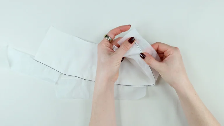 Folding the trimmed hem allowance towards the wrong side before sewing the third stitch on the baby hem in silk georgette