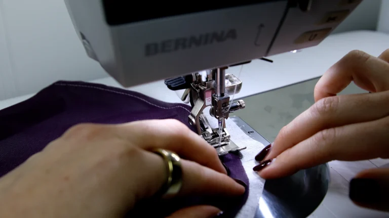 Sewing the first guide stitch for a baby hem on silk georgette using a Bernina sewing machine and tissue paper to stabilse