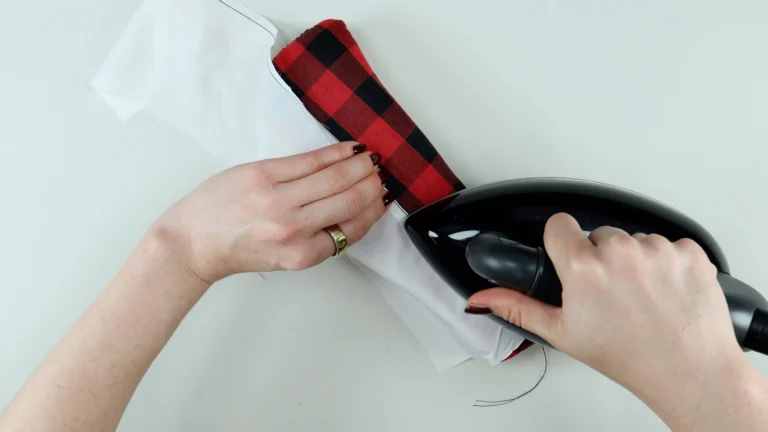 Pressing the hem allowance towards the wrong side of the fabric using a pressing cloth when sewing a baby hem