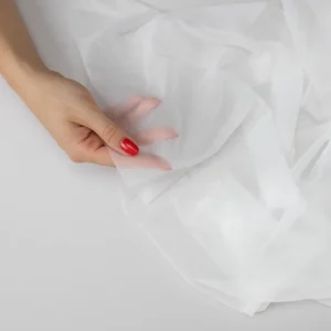 White ultra lightweight couture fusible interfacing held over a hand to show its transparency